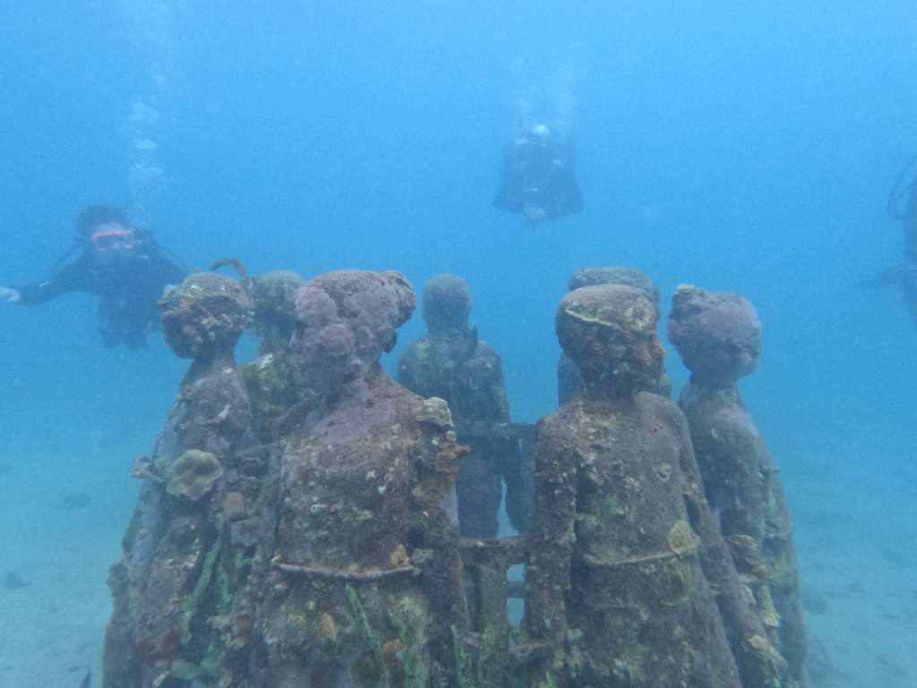 A ring of sculputres underwater with three divers around