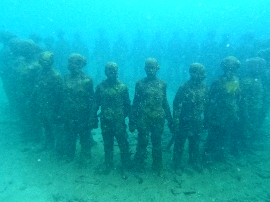 A ring of statues holding hands in murky water at the grenada sculpture park