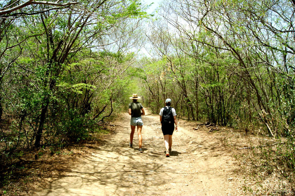 Two woman walking on a dirt road in very dry brush in Grenada