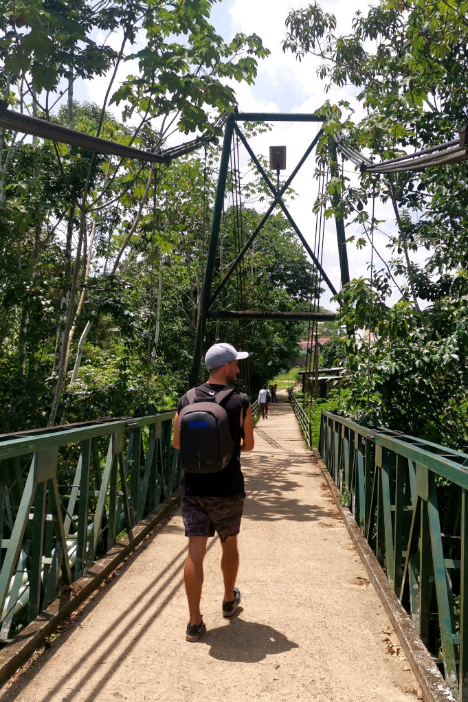 A man walking over a suspension bridge with jungle on either side of him