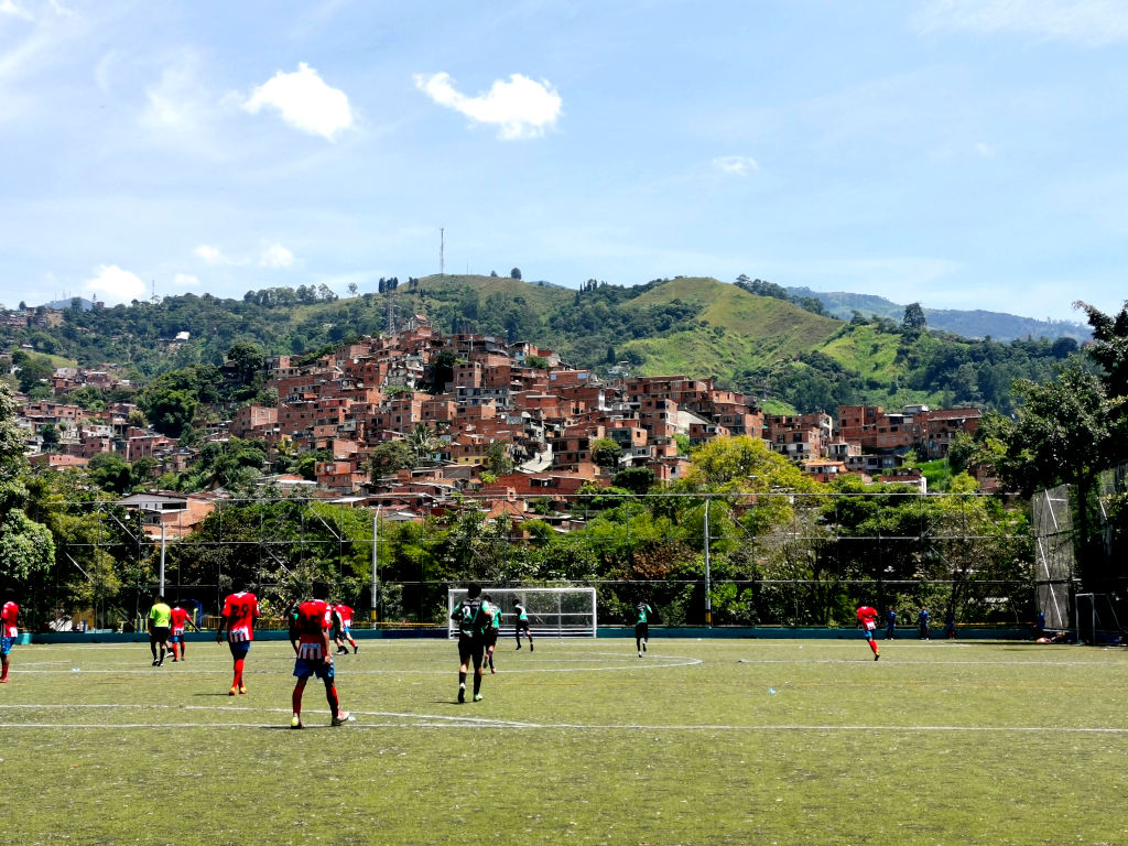 A football field with a collection of buildings on the hill behind it. A good depiction of the Comuna 13 history