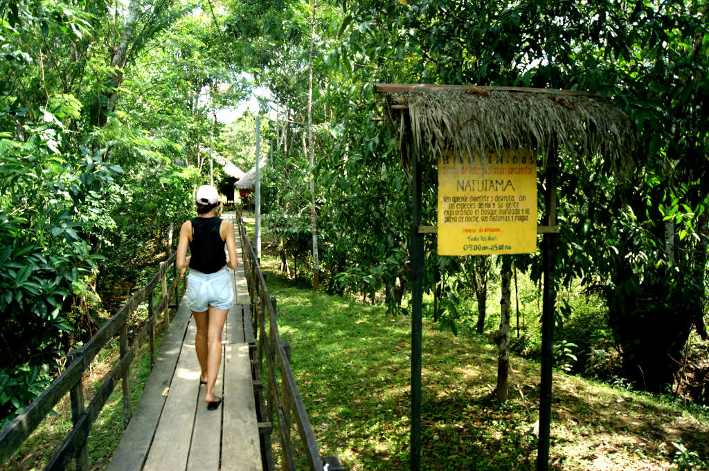 A woman in denim shorts and a black singlet walking along a wooden walkway to a museum in Puerto Narino in the Amazon