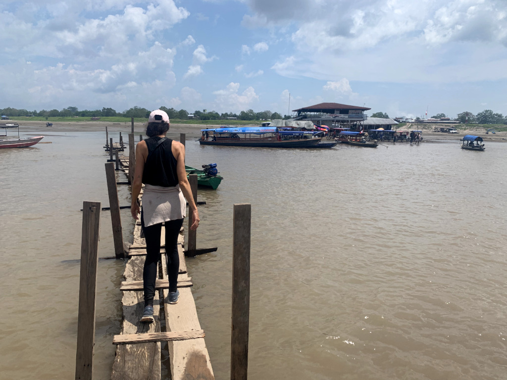 A woman in a black singlet and black leggings walking across a rickety wooden bridge on the way from Leticia to Peru