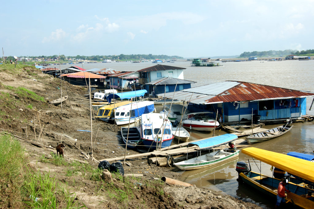A muddy river bank with a collection of boats and houseboats tied to shore by ropes where you can catch a boat from Leticia to Peru