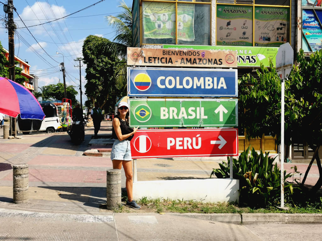 A woman standing next to a sign with directions to Colombia, Brasil and Peru one of the best things to do in Leticia