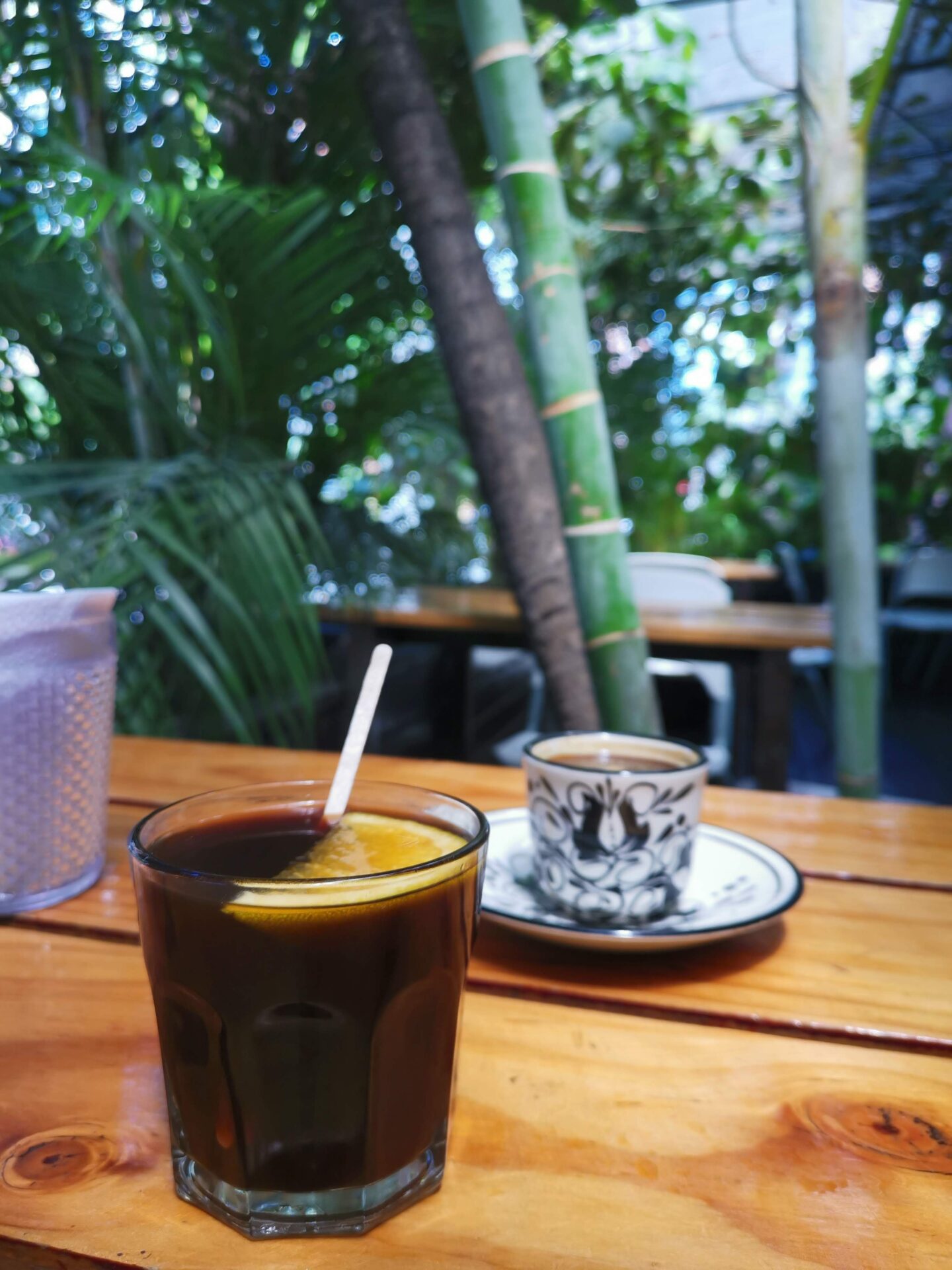 An iced coffee with a slice of orange sitting in it and a black and white coffee mug sitting on the table behind it