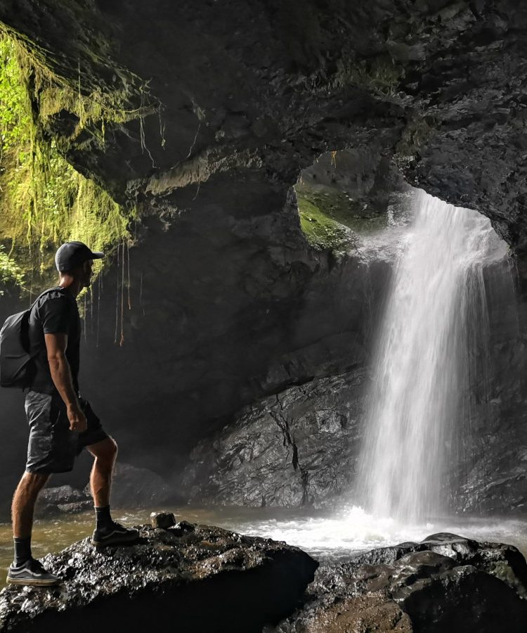 A man standing in front of Cueva del Esplendor gazing at the water pouring through a hole in the top