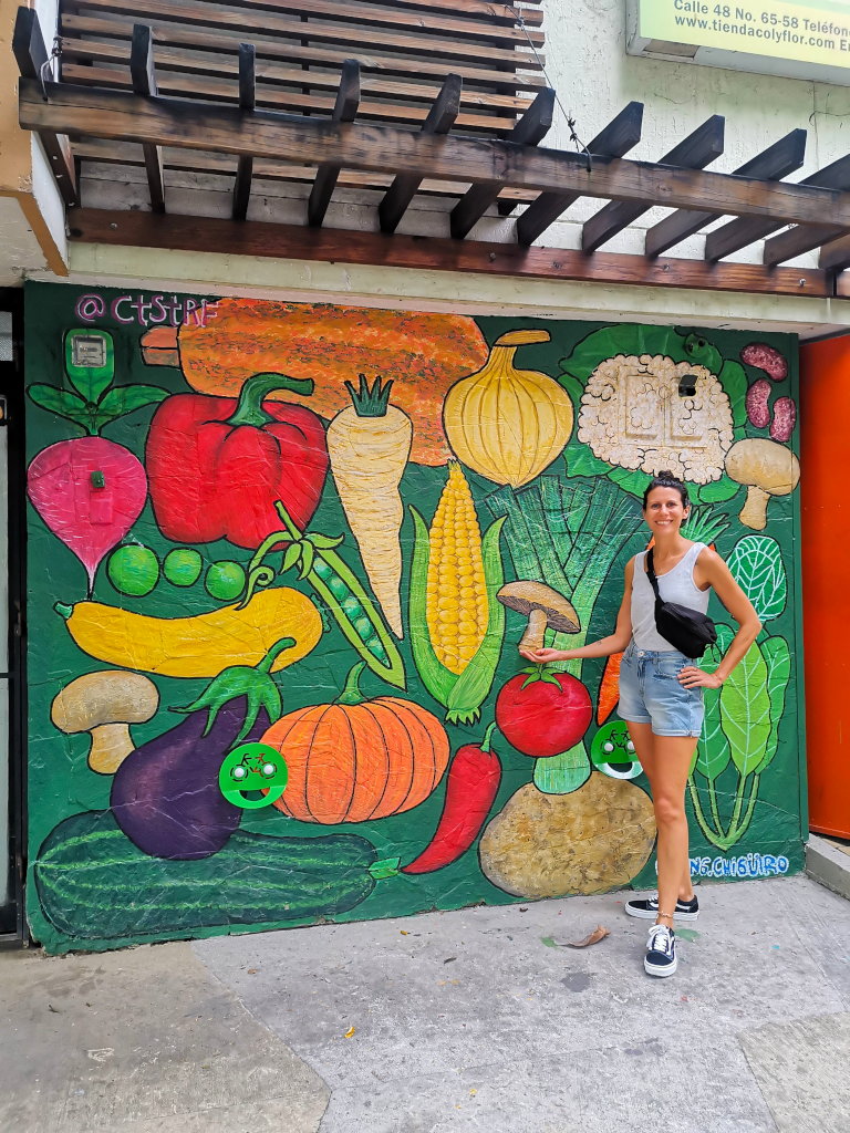 A woman standing in front of a painted mural with veggies on it