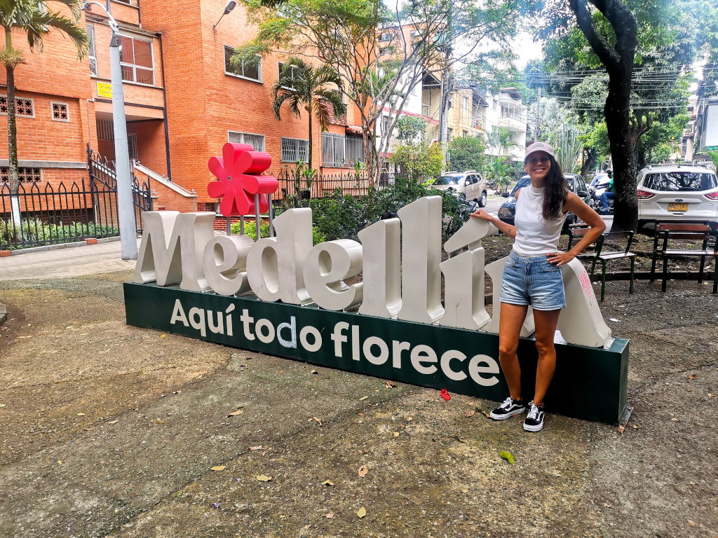A woman standing in front. oga Medellin sign with a flower on top