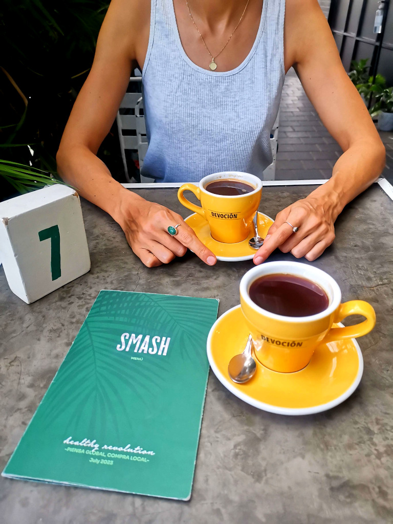 A woman sitting at a cafe with two yellow coffee cups on the table in front of here and a menu on the table