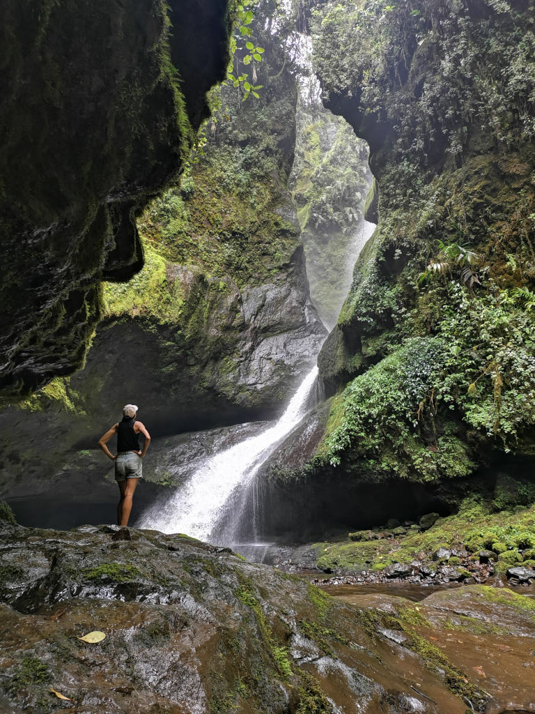 A woman standing with her hands on her hips looking at the Cueva los Guacharos waterfall