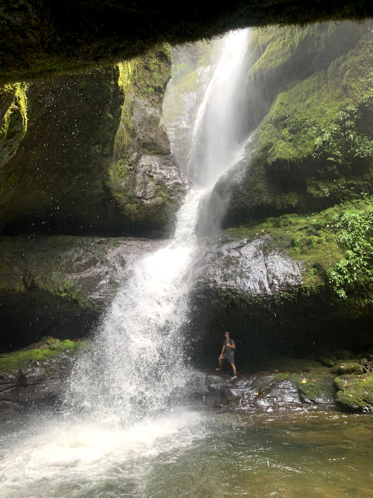 A man standing behind the Cueva los Guacharos waterfall in Jardin Colombia