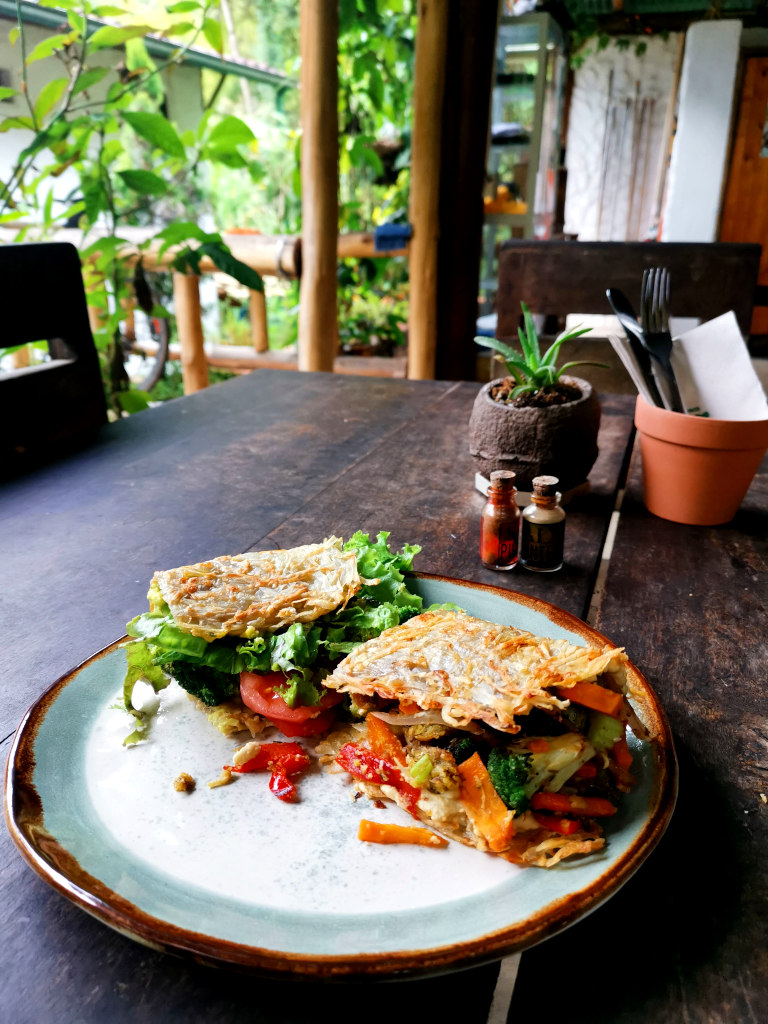 A hashbrown sandwich sitting on a table full of vegetables at Revolucion Bananera a great restaurant in Jardin Colombia
