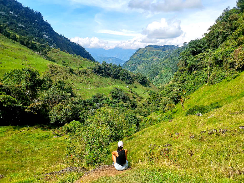 A woman sitting on the ground overlooking a green valley while being on a Jardin hike in Colombia