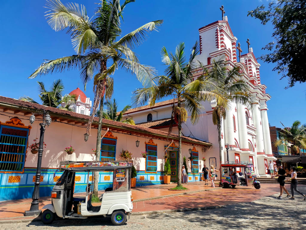 The main church at the Parque Principal de Guatape with a colorful tuk tuk in font of the church one of the best things to do in Guatape