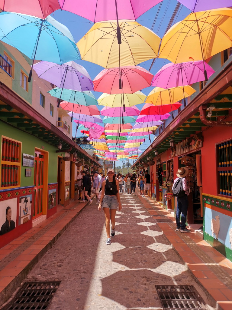 A woman walking through the streets under umbrellas hanging above her, one of the must things to do in Guatape