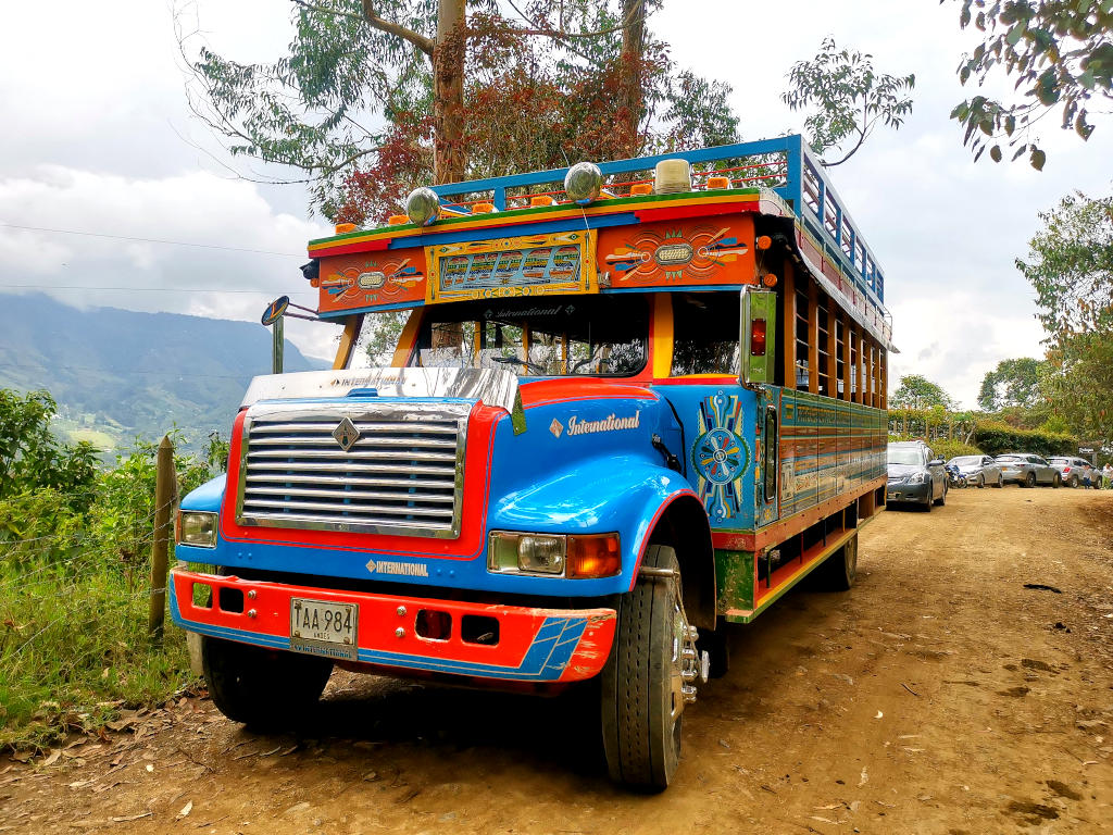 A colorful chiva a bus that is traditionally used in the countryside in Colombia parked on the side of a dirt road near Jardin Colombia