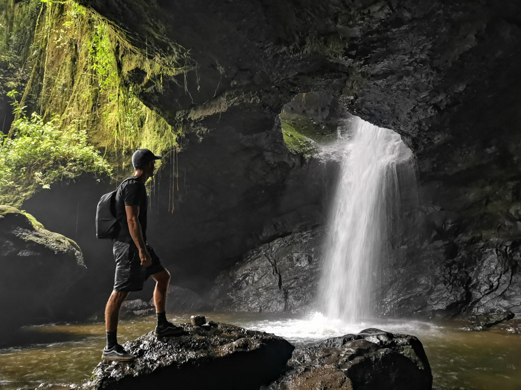 A man standing in front of the Cueva del Esplendor waterfall in Jardin Colombia