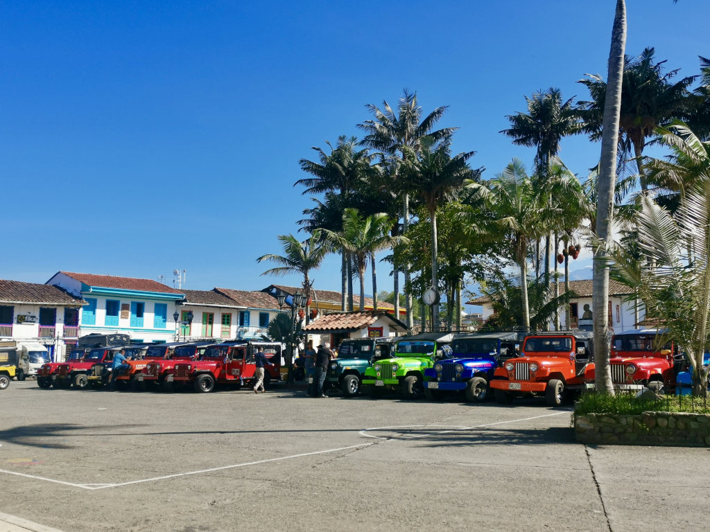 A lineup of of colorful jeeps parked next to a main square with palm trees in the background that is the best way to get from salento to filandia