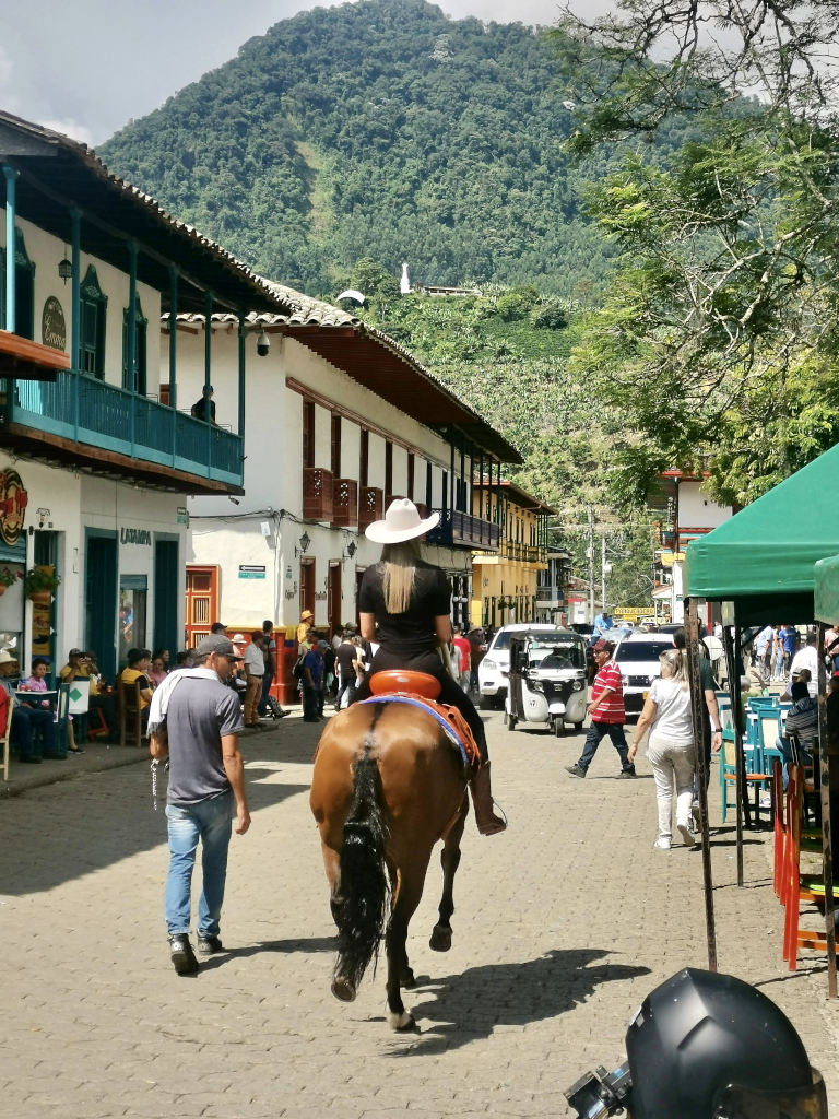 A woman with a cowboy hat riding on a horse through Jardin, Colombia