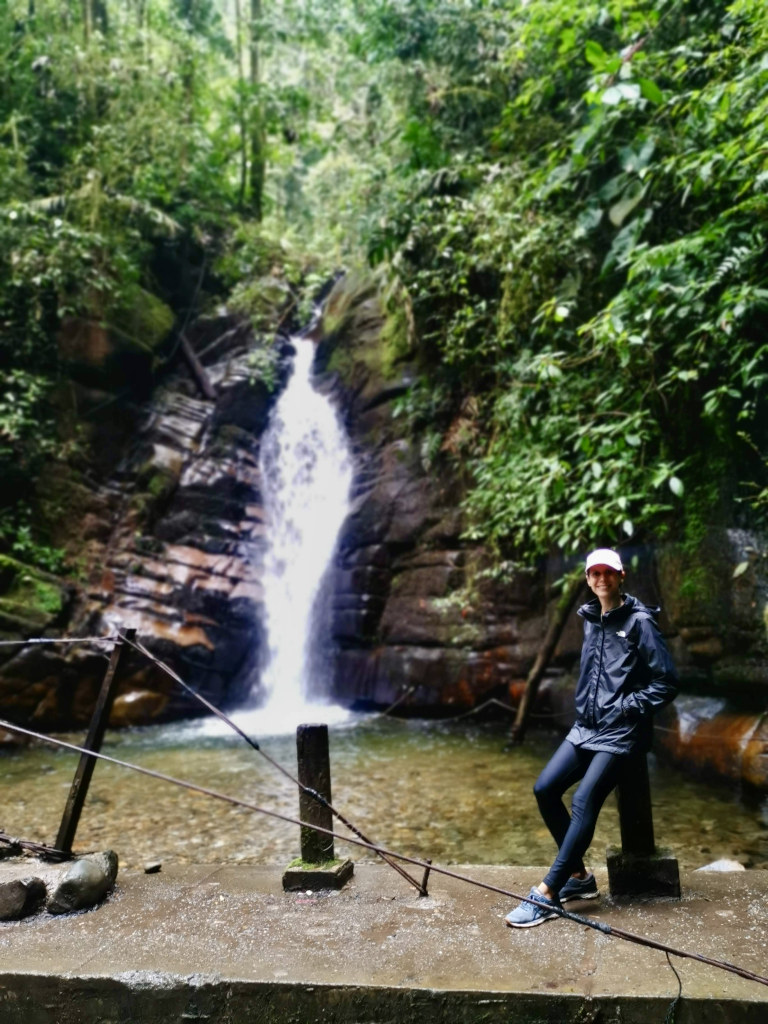 A woman in a black raincoat leaning against a pole in front of the santa rita waterfall which is one of the best things to do in salento colombia