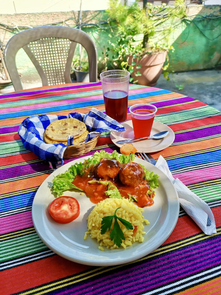 A plate of food with tortillas and a glass of juice next to it on a table at la Casa de las Mixtas a cheap restaurant in Antigua Guatemala
