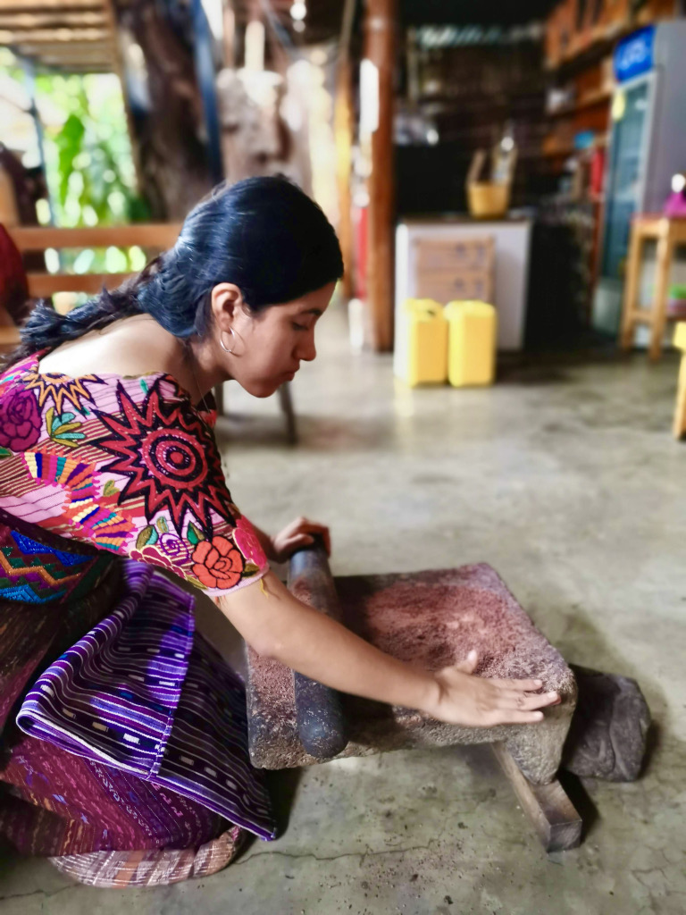 A woman dressed in traditional mayan clothing grinding some cocoa beans using traditional stone tools in San Juan La Laguna Gautemala
