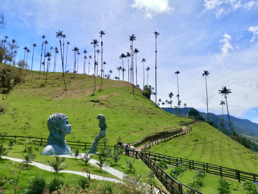 A green hill side covered with very tall wax palm trees and a statue in the foreground at the start of the Cocora Valley hike near Salento Colombia