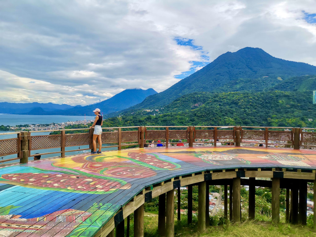 A woman looking out at the view from a mirador over lake atitlan with a couple of volcanoes in the backgroun