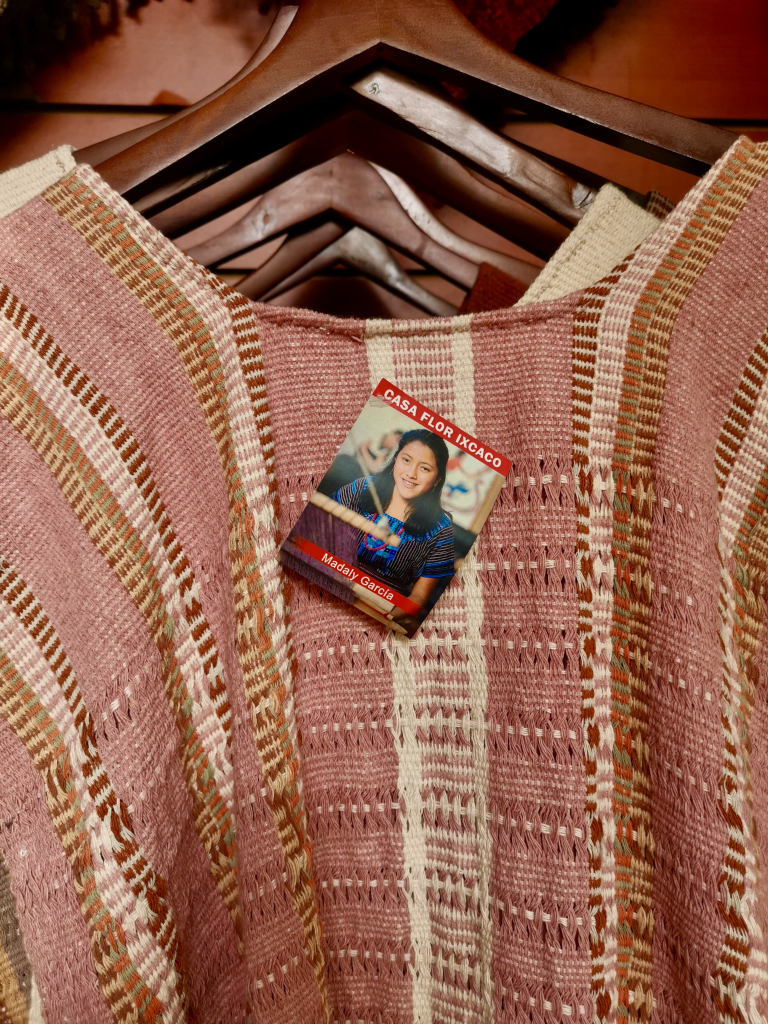 A piece of clothing hanging in a shop with a picture of the mayan woman who made the clothing hanging from it