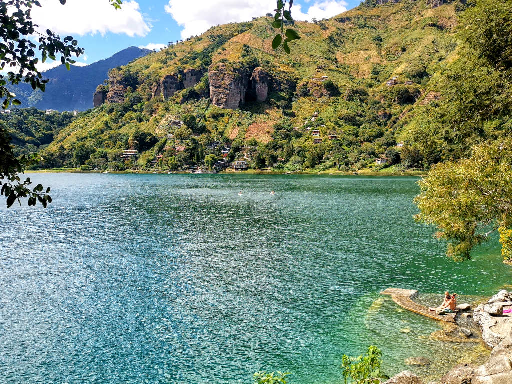Two people sitting on rocks beside clear water at lake atitlan in guatemala