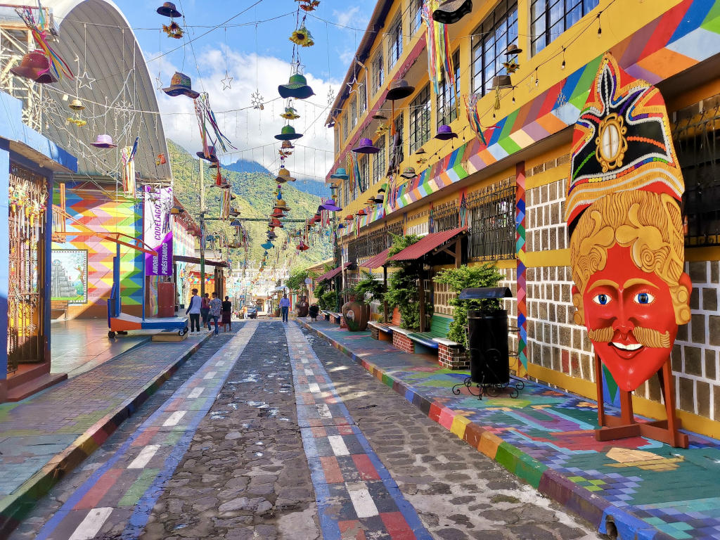 A colorful street with paintings on the ground and on the walls with hats hanging in the air