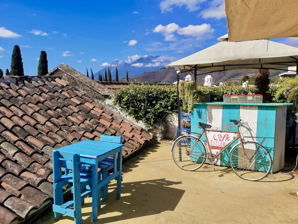 A rooftop cafe in Antigua Guatemala with a bicycle in front of a blue desk and volcanos in the background