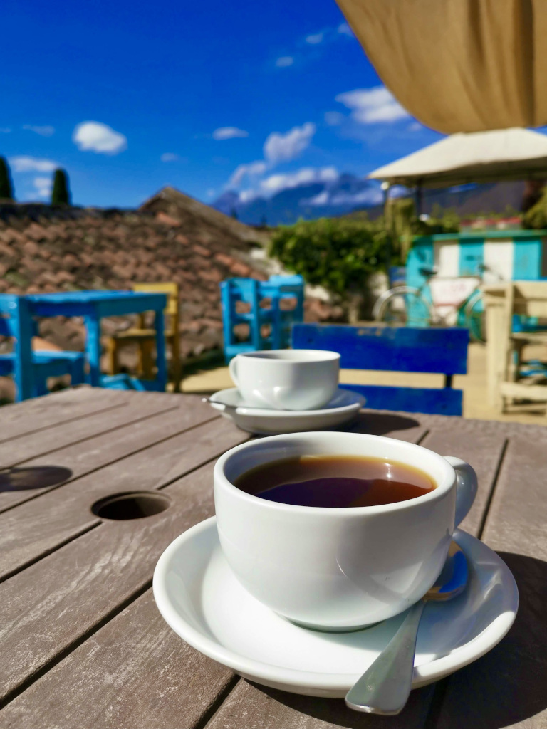 A cup of coffee sitting on a table with a volcano erupting in the background in Antigua Guatemala