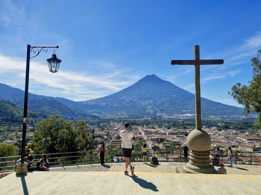 A man in a white tshirt standing in front of a cross looking at volcan Agua in Antigua Guatemala