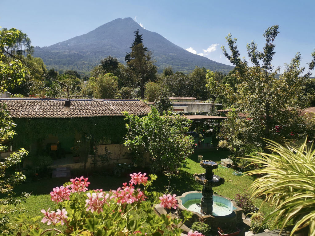 Overlookign a beautiful garden with pink flowers and Volcan Agua in the back 