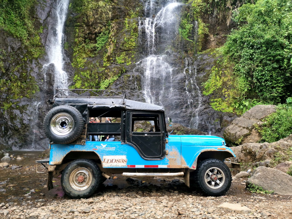 A blue jeep parked in front of a waterfall