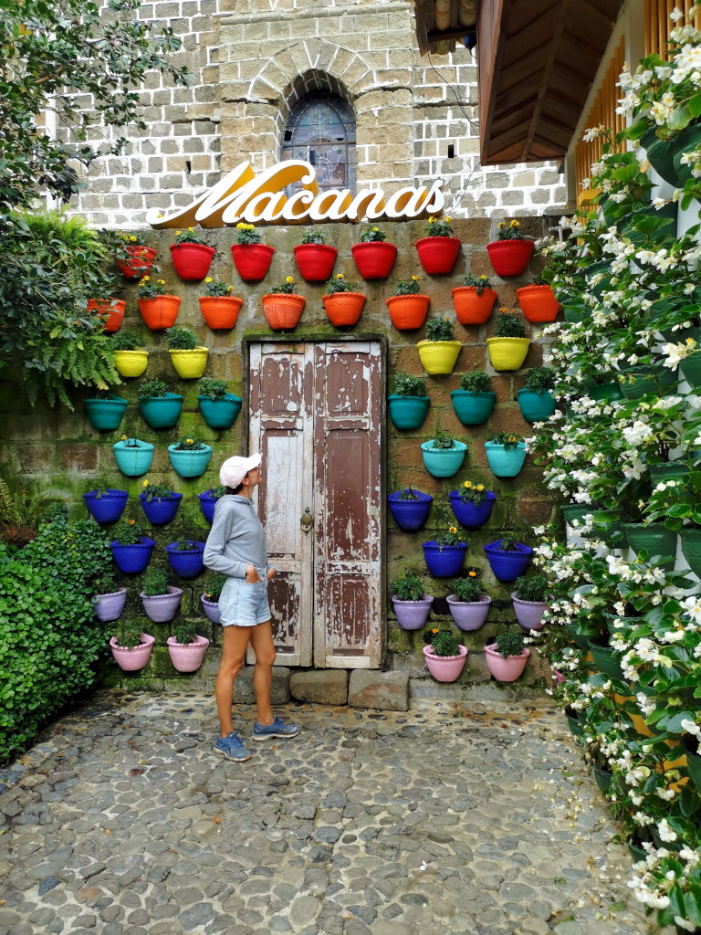A woman standing in front of a wall with colorful flower pots inside one of the best cafes in Jardin Colombia