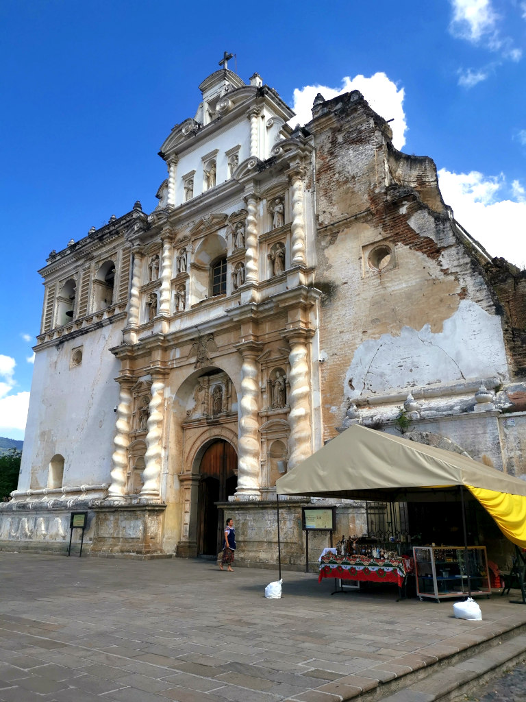 A woman dressed in traditional clothing walking in front of a church in Antigua Guatemala