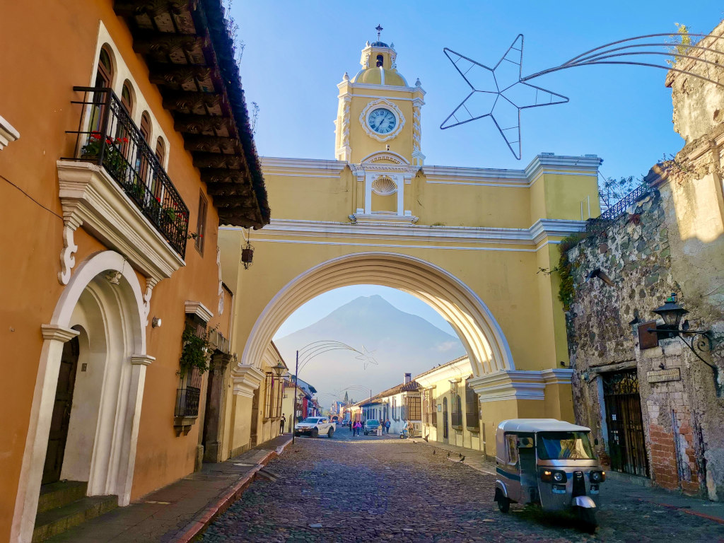 A tuk tuk driving down a cobblestone street underneath the Santa Catalina Arch in Antigua Guatemala