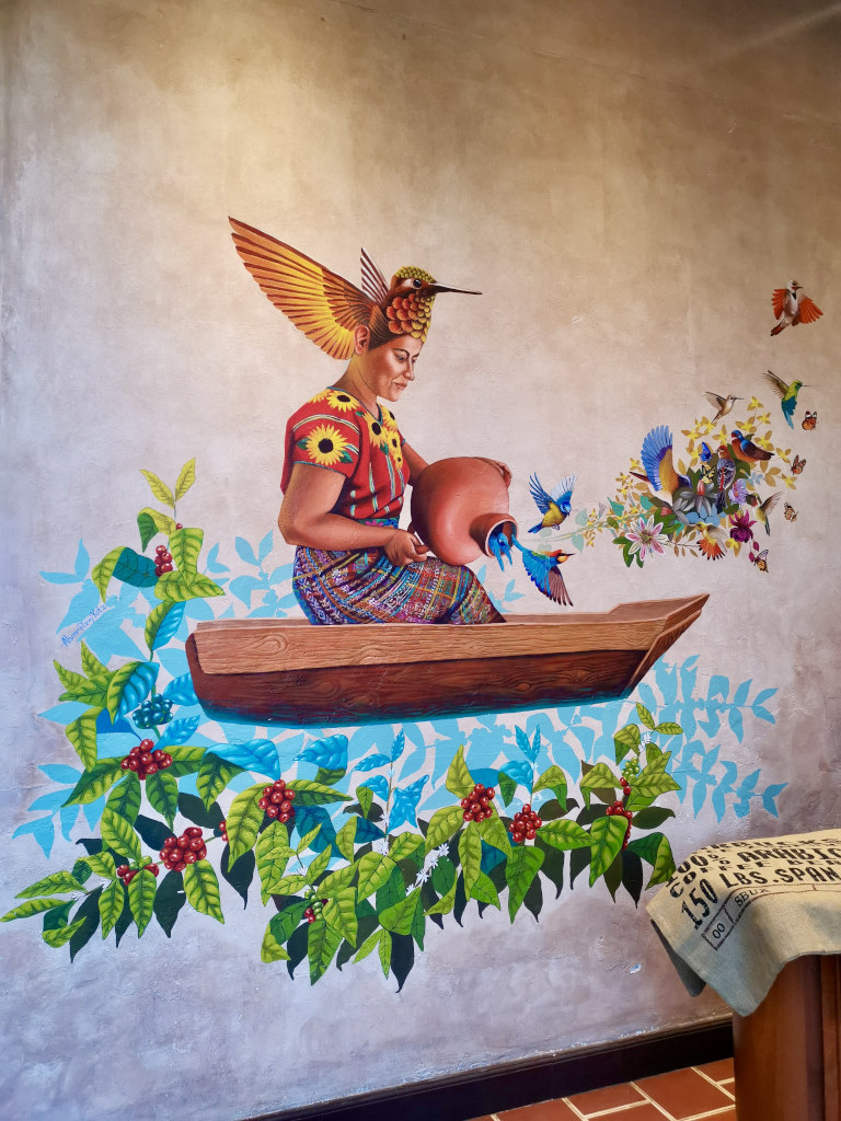 A mural of an indigenous Guatemalan women in a boat with red grapes around here