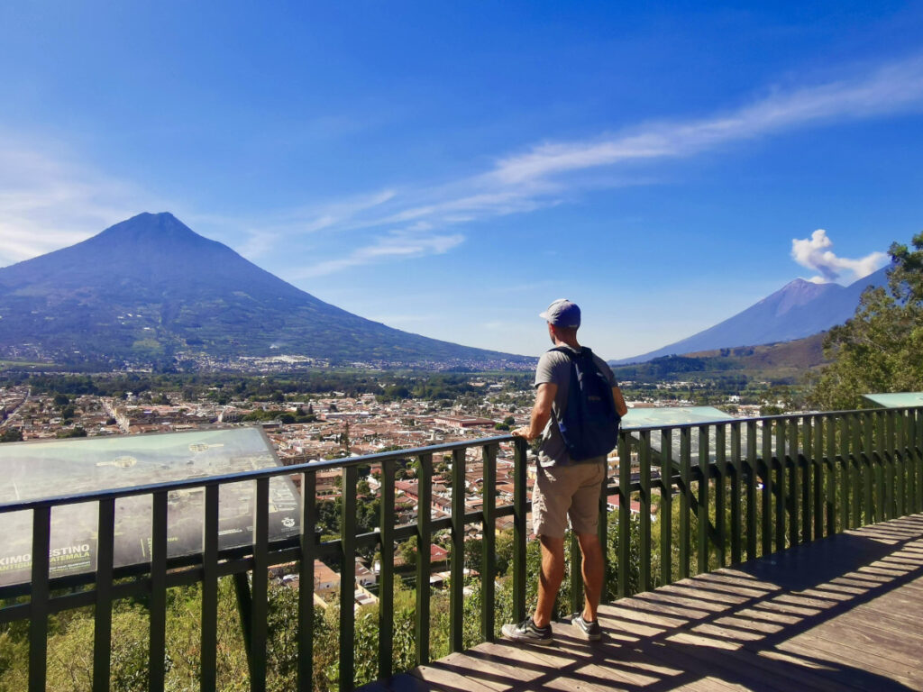 A man looking over the town of Antigua with volcanoes in the back from the Cerro de la Cruz lookout point - one of the best cheap things to do in Antigua Guatemala