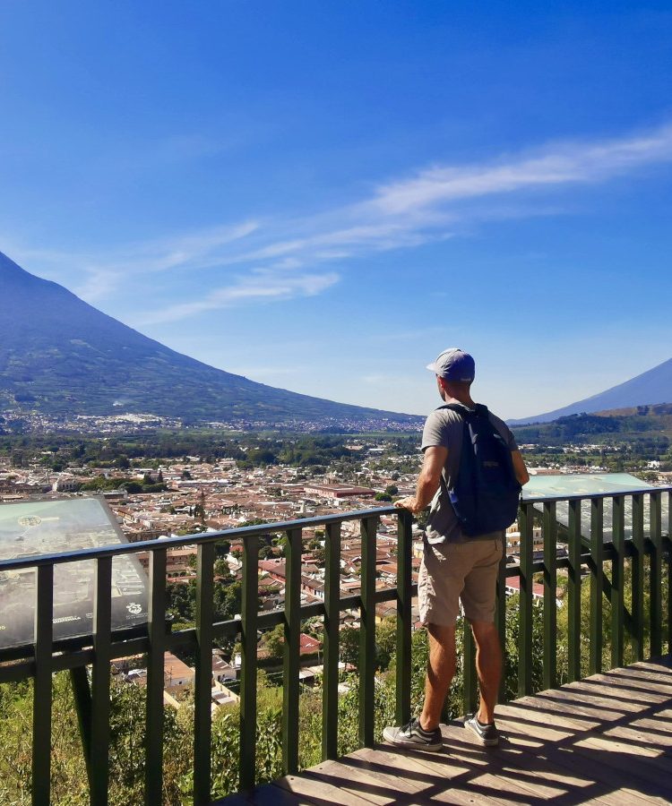 A man looking over the town of Antigua with volcanoes in the back from the Cerro de la Cruz lookout point - one of the best cheap things to do in Antigua Guatemala