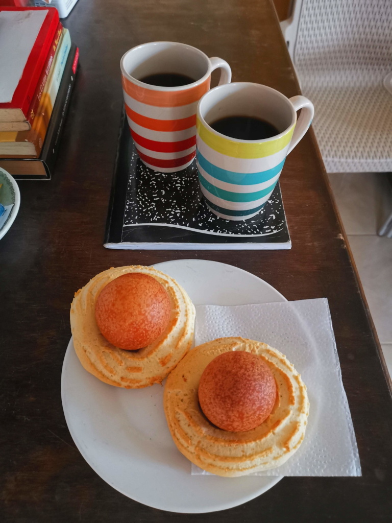 Two cups of coffee next to bunelos on a plate, a traditional Colombian breakfast