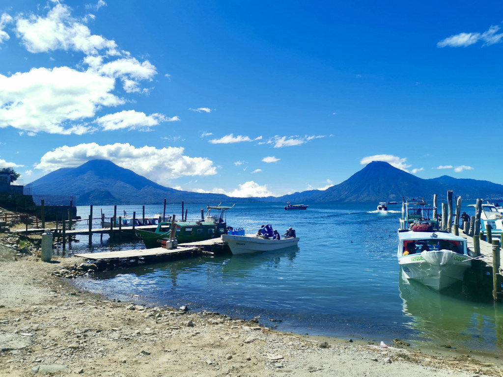 Two boats sitting next to some wooden docks with two volcanoes in the background