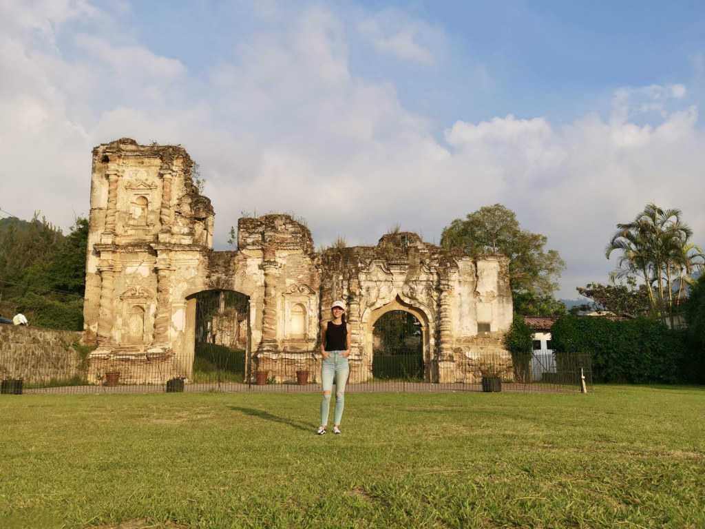 A woman standing on a grassy field in front of the some ruins in Antigua Guatemala