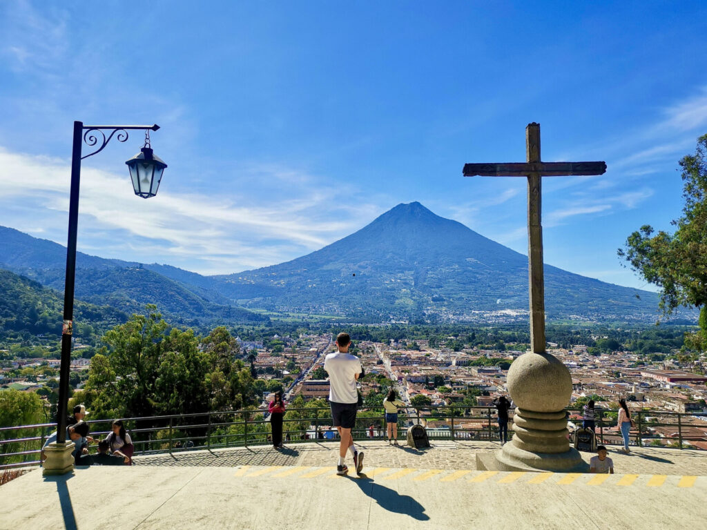 A man standing next to a large cross enjoying the view at the cerro de la cruz in antigua guatemala