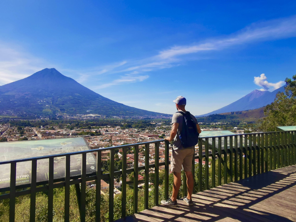 A man enjoying the view from the Cerro de la Cruz in Antigua Guatemala while Fuego volcano erupts in the distance