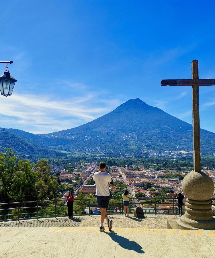 A man standing on top of Cerro de la Cruz overlooking Antigua Guatemala with volcanoes in the back