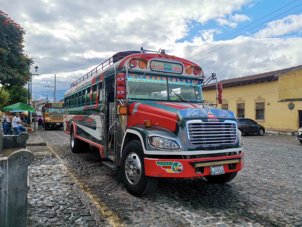 A colorful chicken bus driving down a cobblestone street from Antigua Guatemala to Lake Atitlan